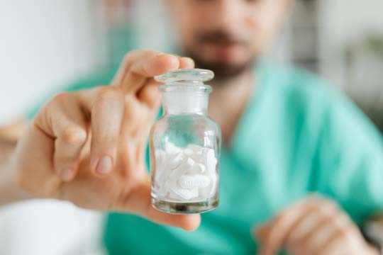 A man holding a glass jar filled with white pills